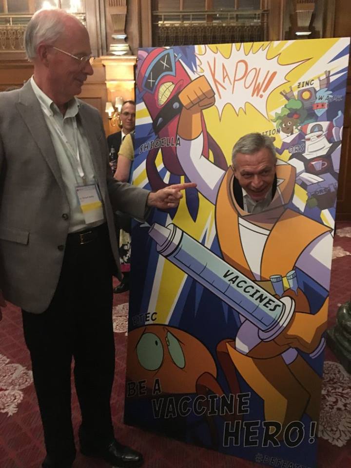Dr. Walker pointing to Dr. Bourgeois posing in a vaccine superhero cutout