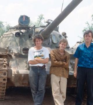Three men stand against a military tank 