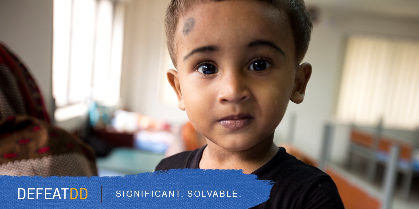 A young child with short hair and a solemn expression looks directly at the camera. The background is softly blurred, showing an indoor setting with light coming through windows. The text "DEFEATDD" and "SIGNIFICANT. SOLVABLE." is written over a blue brushstroke at the bottom.