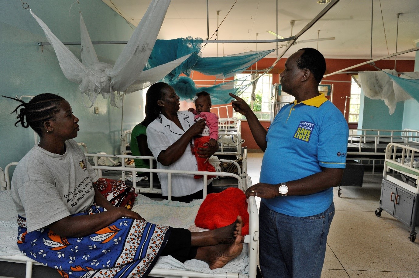 A female healthcare worker makes rounds at a hospital: a patient is sitting up in a hospital bed. 