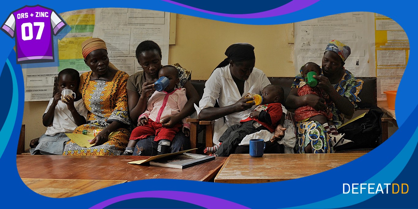 Women seated on a bench hold babies as they drink from cups. The setting appears to be a waiting room with informational posters on the wall. A colorful border with "ORS + Zinc 07" and "DefeatDD" surrounds the image.