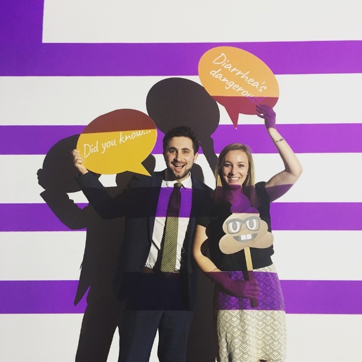 Man and woman in front of purple and white striped wall holding poo emoji and "Diarrhea's dangerous" conversation bubble