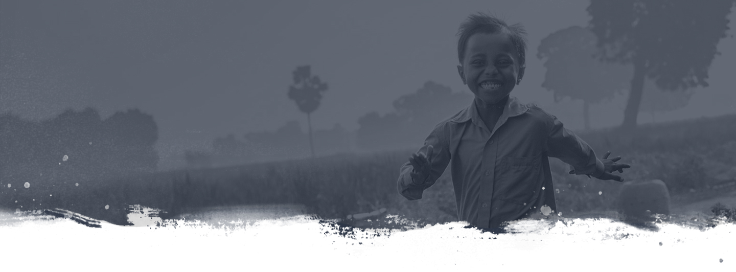 A young child, smiling brightly, runs through a foggy field. The image is in grayscale with an artistic white paintbrush effect along the bottom edge. Trees and misty landscape form the background.