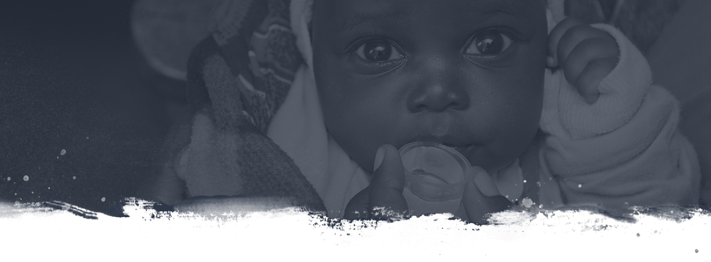 A monochrome close-up of an infant with wide, expressive eyes, holding onto a small clear cup while lying on a blanket. The image has a grunge-style white paint effect at the bottom.