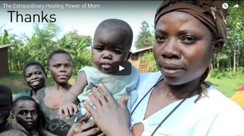 A woman wearing a headscarf holds a baby while five other children stand nearby, smiling. They are outdoors in a rural area with greenery and houses in the background. Text in the image reads "The Extraordinary Healing Power of Mom" and "Thanks.