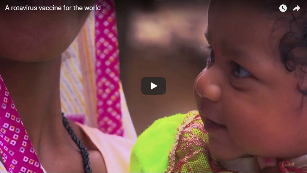 A close-up of a baby in colorful clothing being held by an adult. The baby is looking up with a curious expression. The image has a caption that reads, "A rotavirus vaccine for the world.