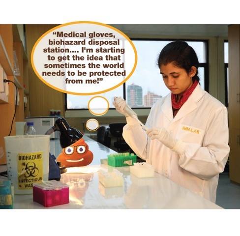 A lab technician wearing a lab coat and gloves is working at a lab station. A thought bubble next to her says, "Medical gloves, biohazard disposal station... I'm starting to get the idea that sometimes the world needs to be protected from me!" A smiley face toy lamp is on the desk.