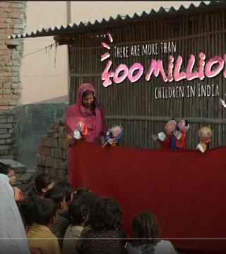 A woman in a pink headscarf entertains a group of children with a puppet show in front of a modest brick and bamboo structure. The text above reads, "There are more than 400 million children in India.