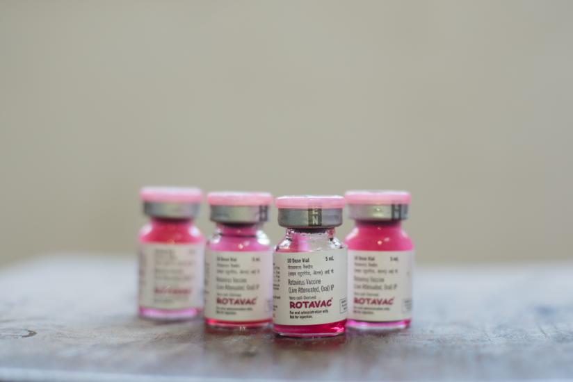 Four vials labeled "ROTAVAC" are arranged on a surface. The vials contain a pink-colored liquid and have gray caps. The labels display dosage information and other text, though it is not fully legible in the image. The background is neutral and out of focus.