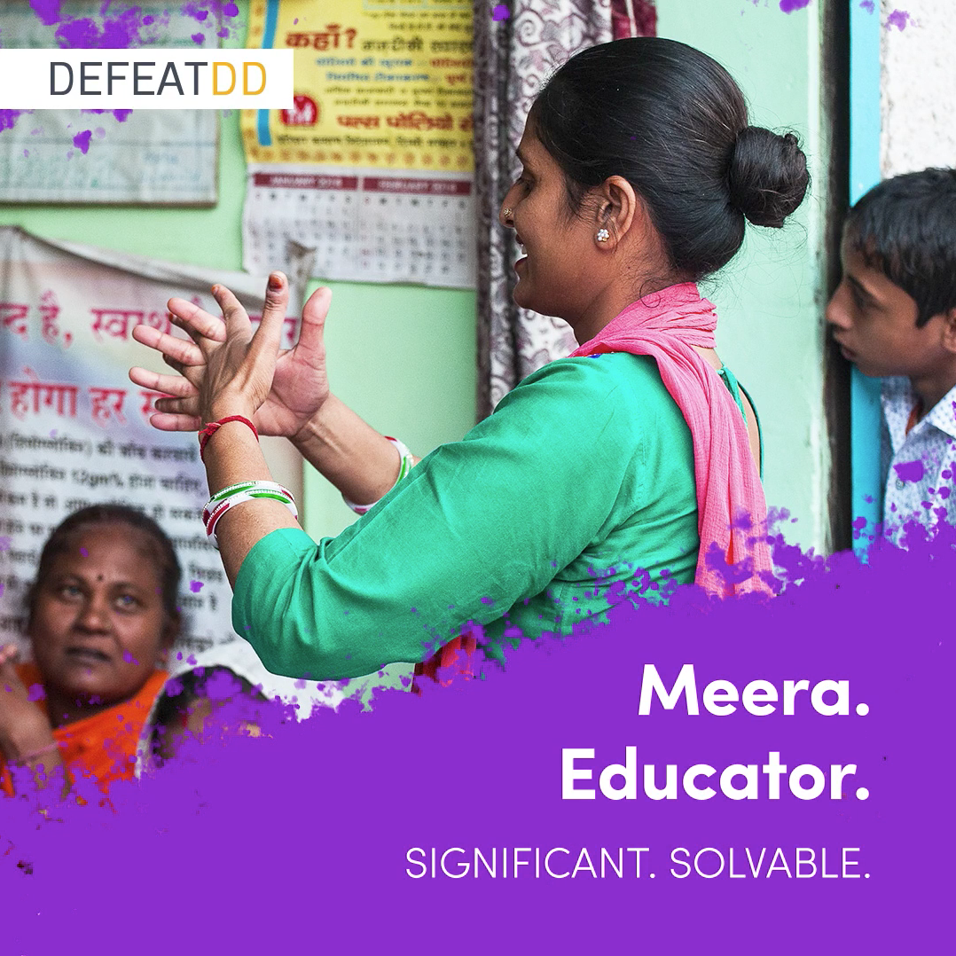 A woman, labeled as Meera and an educator, is speaking to a small group of people, including a seated woman in a red sari. The text on the image reads "DEFENDDD" at the top, with "Meera. Educator. Significant. Solvable." at the bottom.