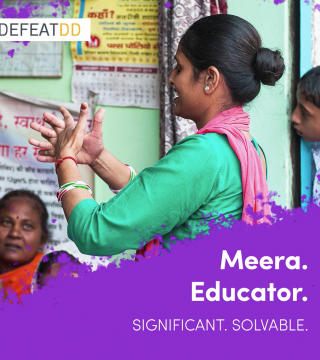 A woman in a green and red outfit educates a small group, using hand gestures. She is in a room with posters on the wall. A seated older woman and a child are visible. The text reads: "Meera. Educator. Significant. Solvable." with a "DefeatDD" logo.