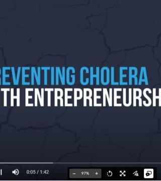 A video screenshot with the text "Preventing Cholera With Entrepreneurship" displayed in blue and white against a dark, cracked background. The video player controls are visible at the bottom, showing a duration of 1:42 and the video is at the 0:05 mark.