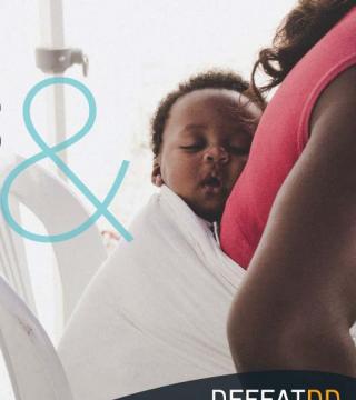 A baby sleeps peacefully while being carried on a woman's back in a white cloth. The baby has curly hair, and the woman is wearing a red top. There is part of a blue ampersand symbol visible on the image along with text at the bottom that reads "DEFEATDD.