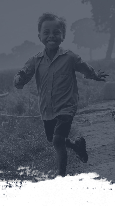 A joyful child with short hair is running along a path, wearing a buttoned shirt and shorts. Trees and grass are in the background, and the image has a grayscale filter.